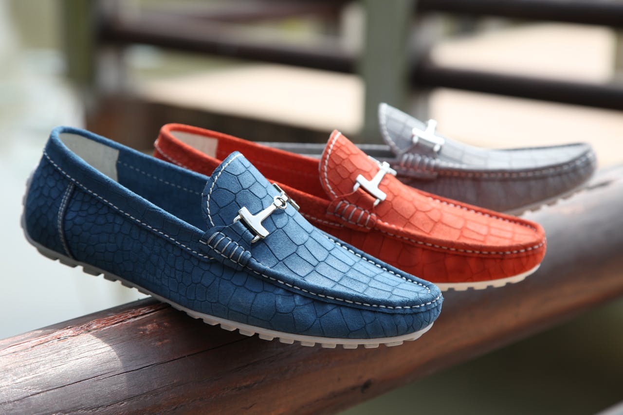 heros-img Fashionable leather loafers in various colors displayed on a wooden railing outdoors.
